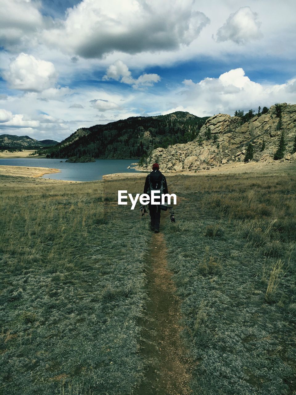 Rear view of man with backpack walking on landscape against sky