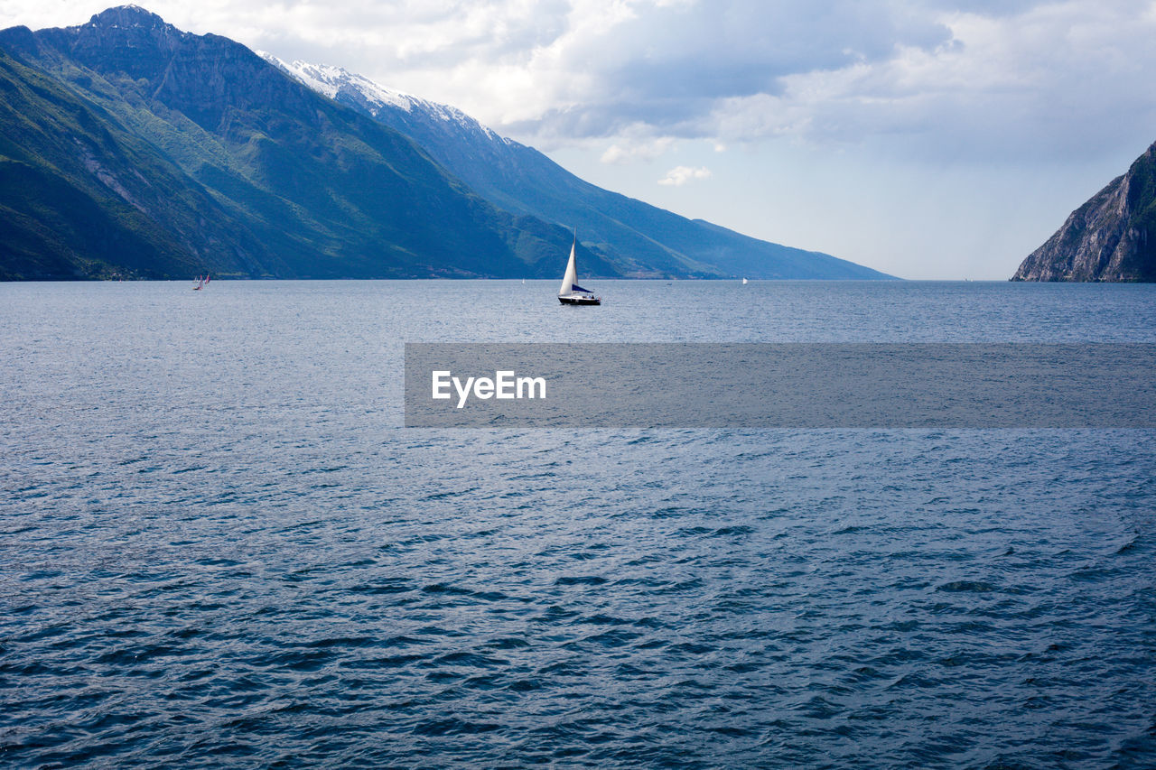 Sailboat in lake garda with mountains against sky