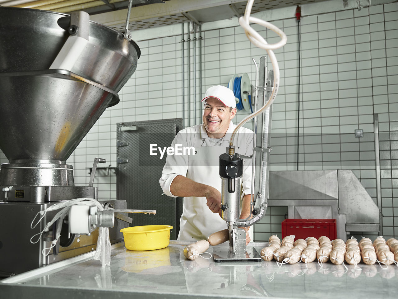 Happy butcher making sausages through machinery at factory