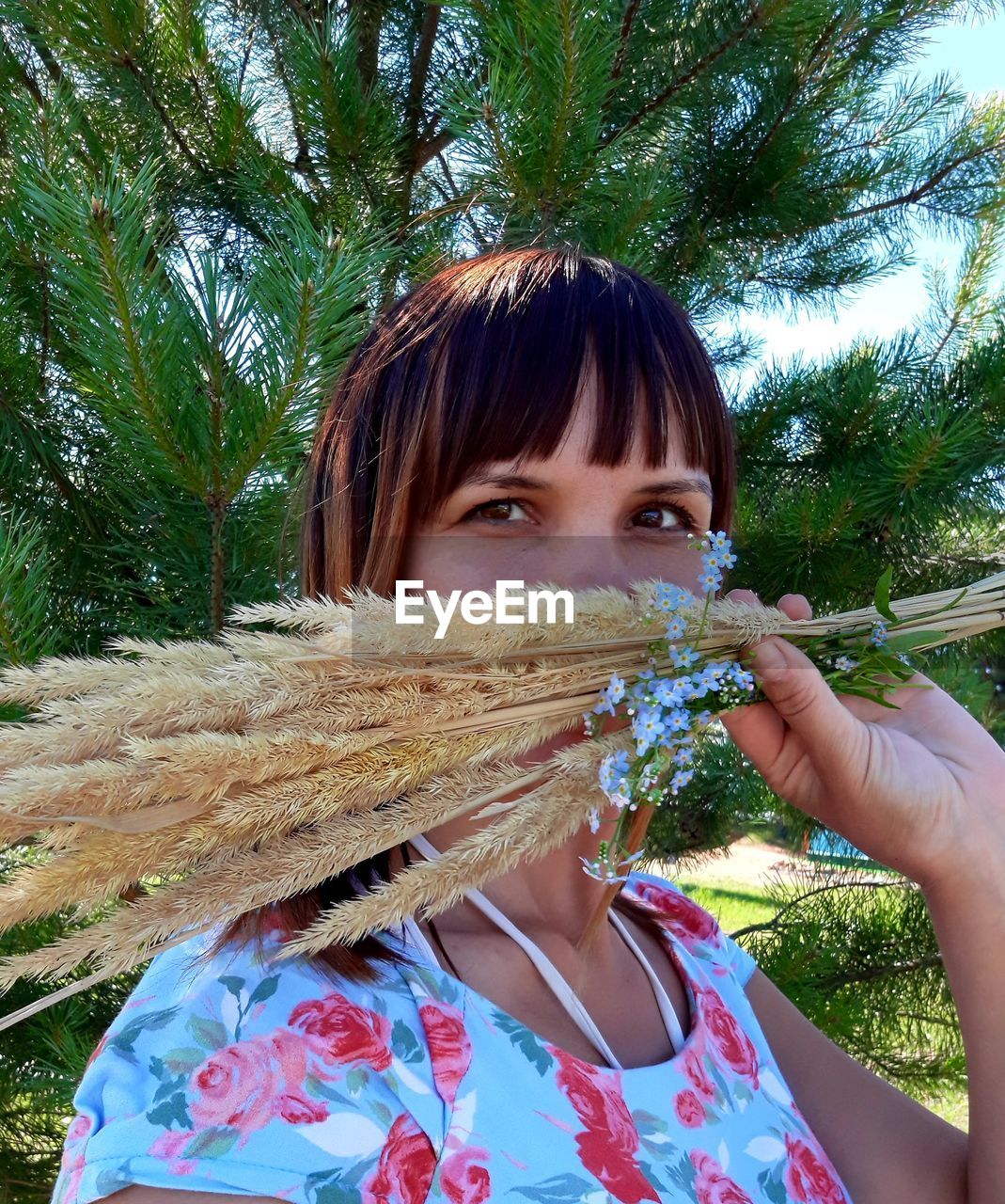 Portrait of woman holding plant against trees