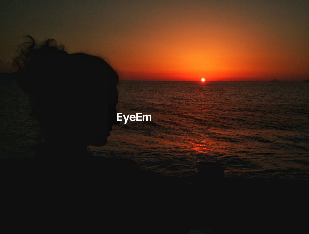 SILHOUETTE WOMAN STANDING ON BEACH AGAINST ORANGE SKY