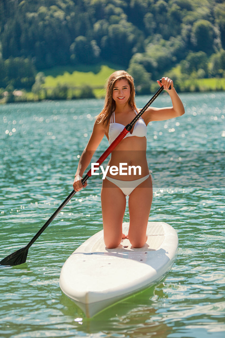 Full length of young woman paddleboarding in lake