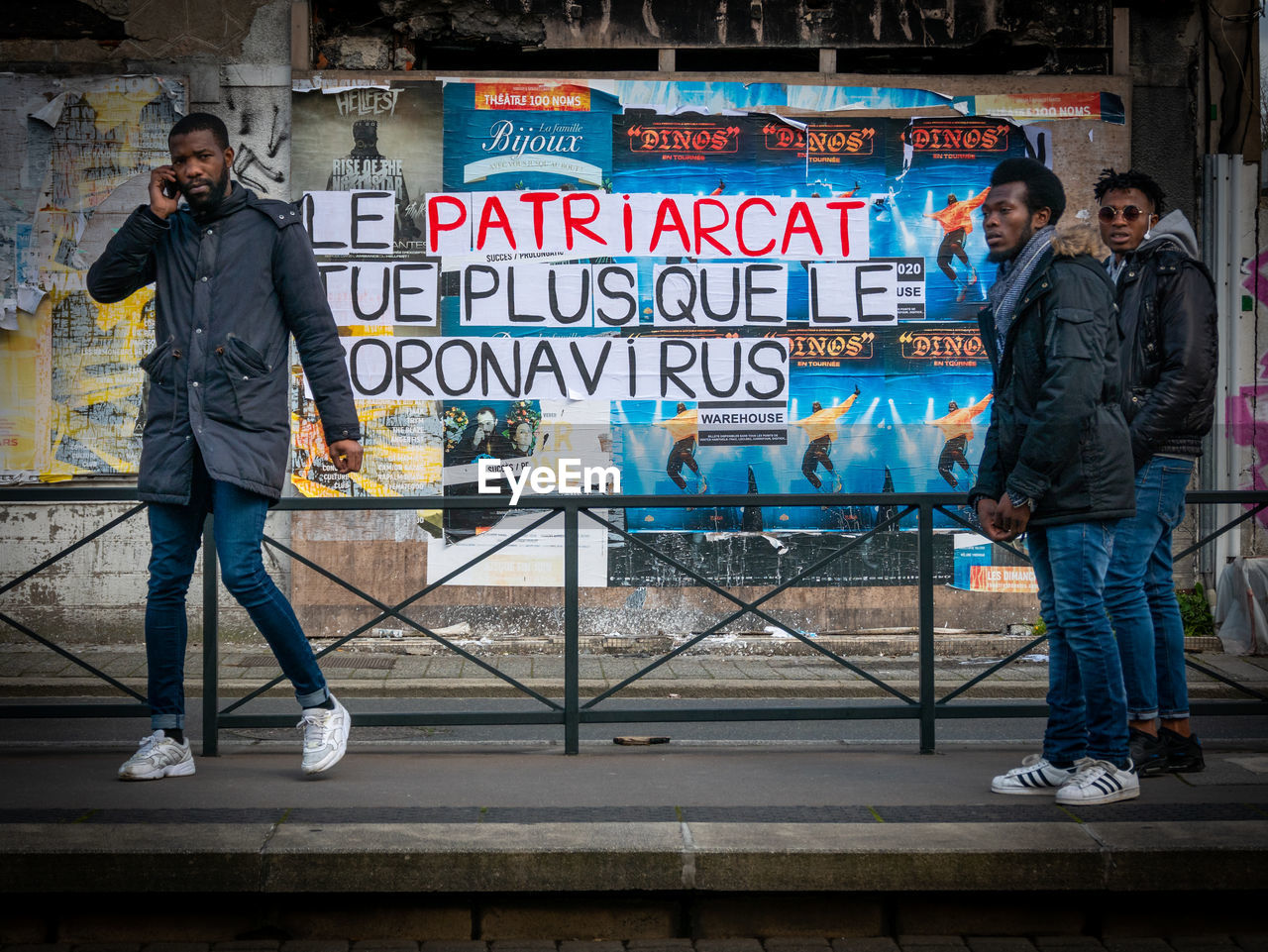 FULL LENGTH PORTRAIT OF MAN STANDING AGAINST GRAFFITI ON CITY