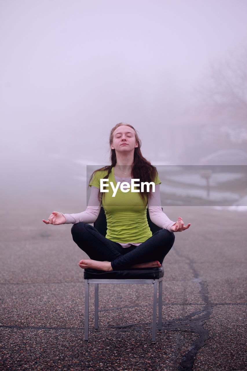 Beautiful young woman doing yoga on chair during foggy weather