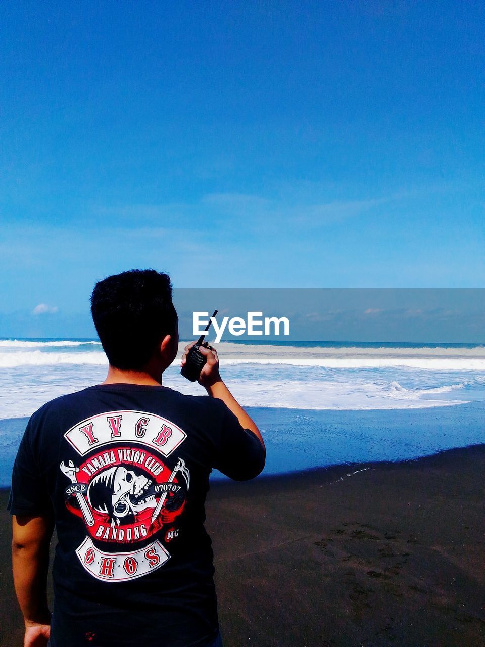 REAR VIEW OF MAN STANDING AT BEACH