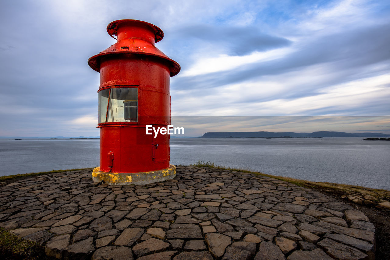 Red lighthouse atop the headland of the sugandisey peninsula on stikkysholmur harbor in west iceland