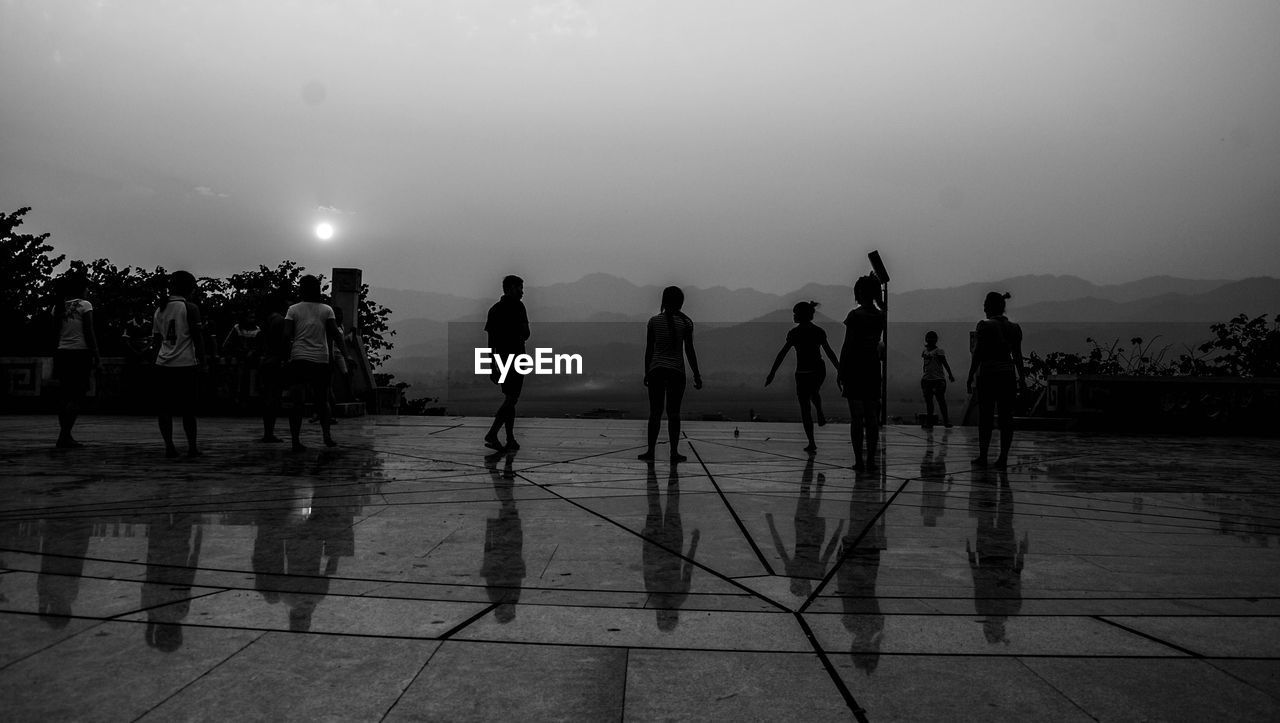 SILHOUETTE PEOPLE STANDING ON BEACH AGAINST SKY DURING SUNRISE