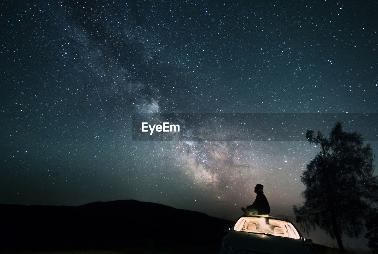 Austria, mondsee, silhouette of man sitting on car roof under starry sky