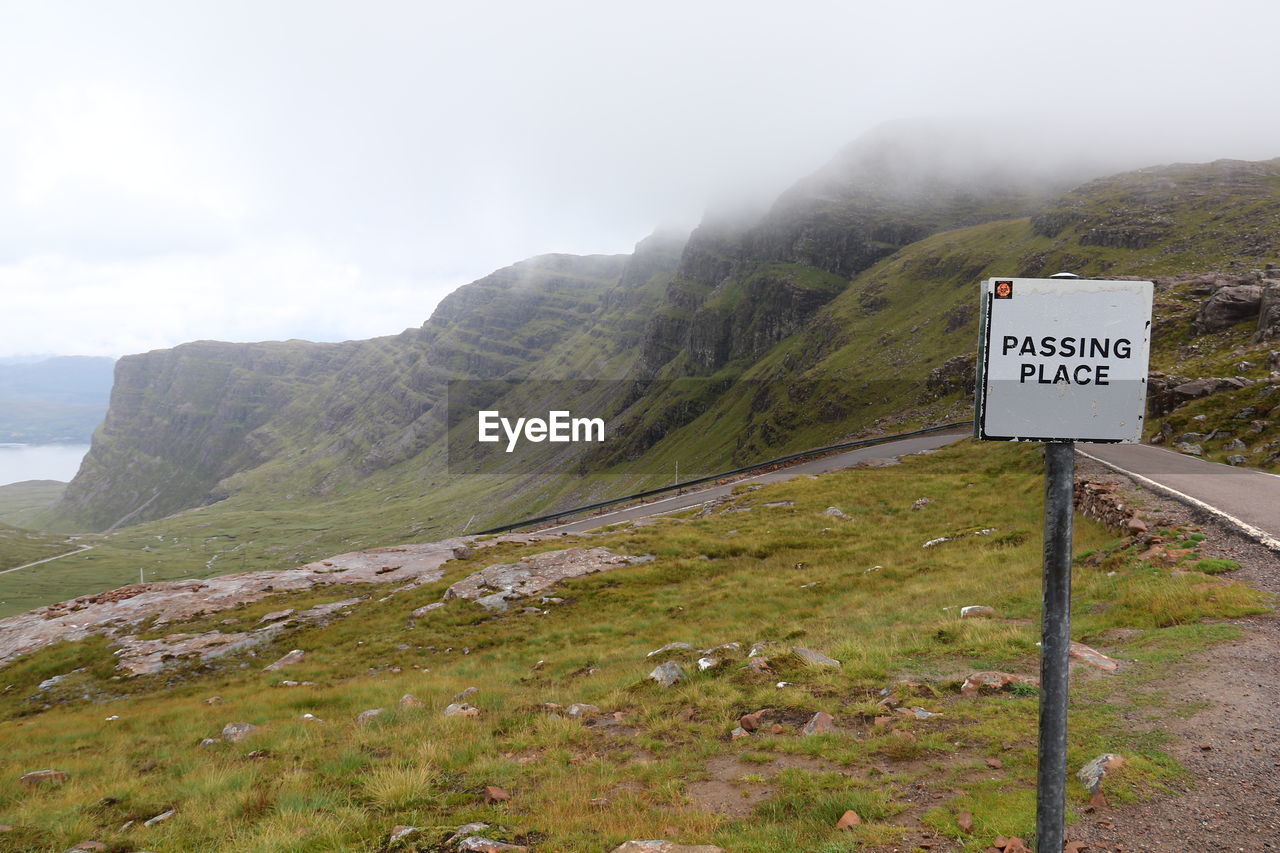 ROAD SIGN ON LANDSCAPE AGAINST MOUNTAINS