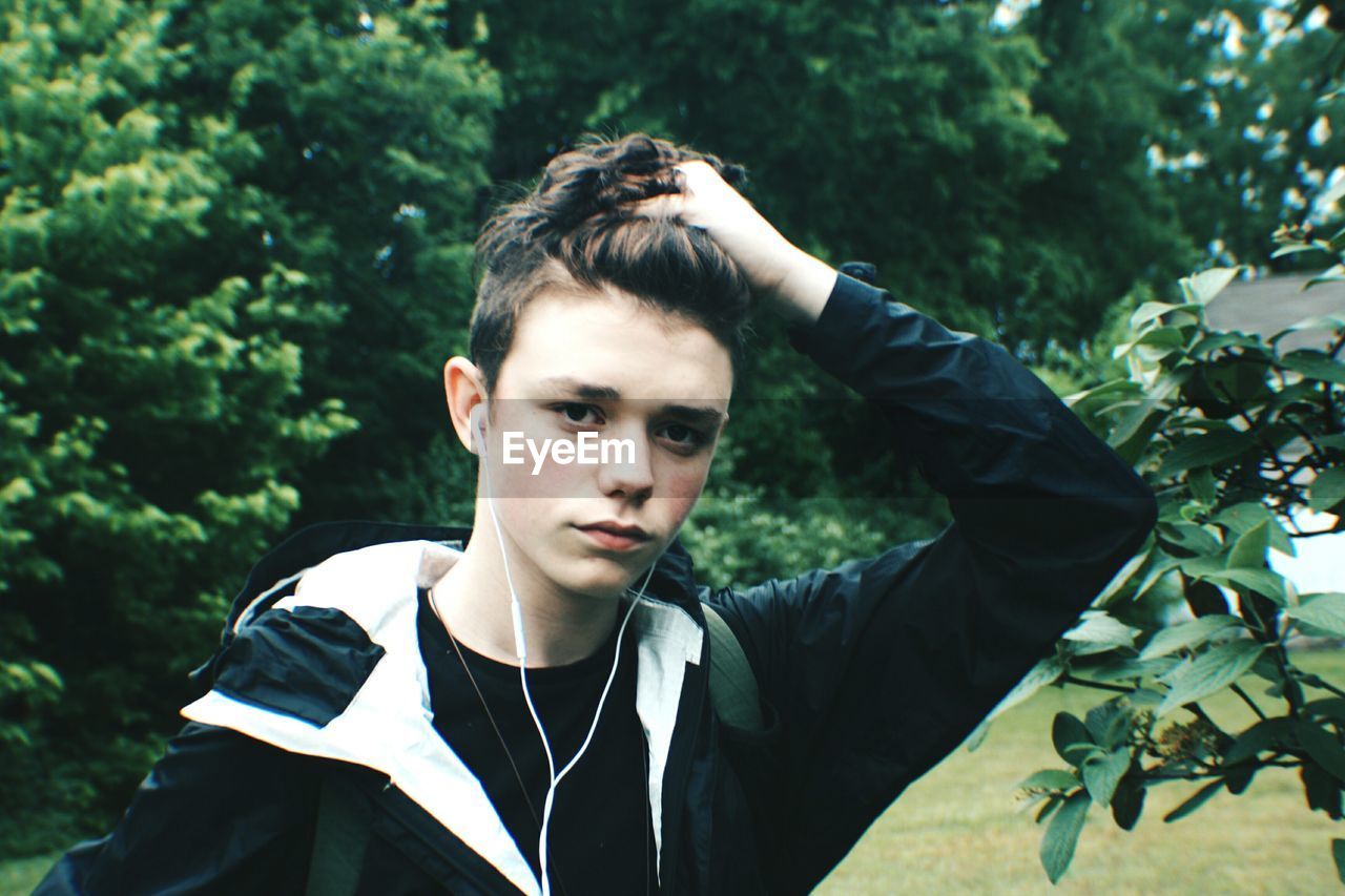 Portrait of boy with hand in hair against trees