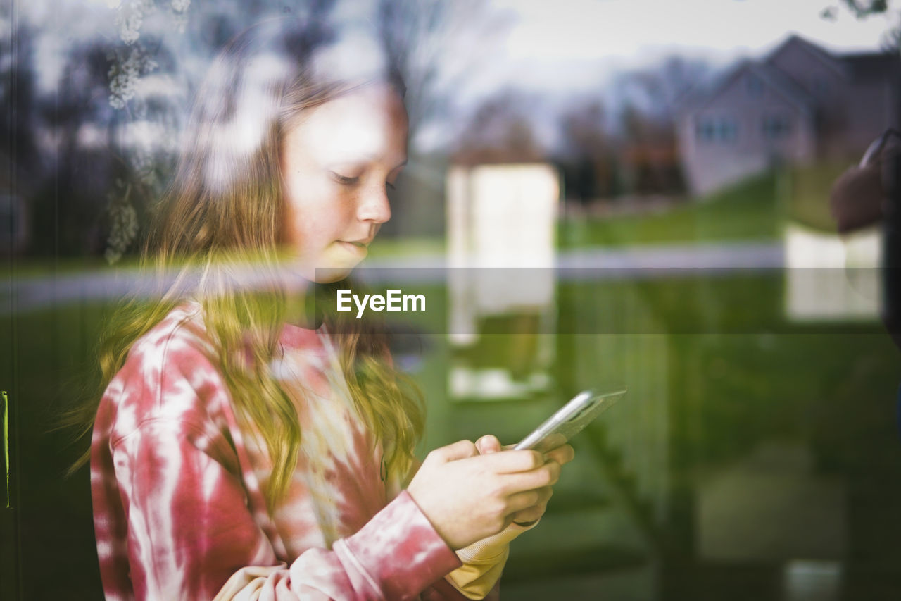 Girl using smart phone seen through window