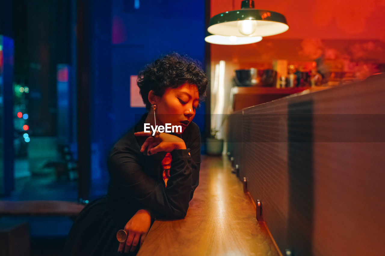 Woman looking away while sitting in illuminated building