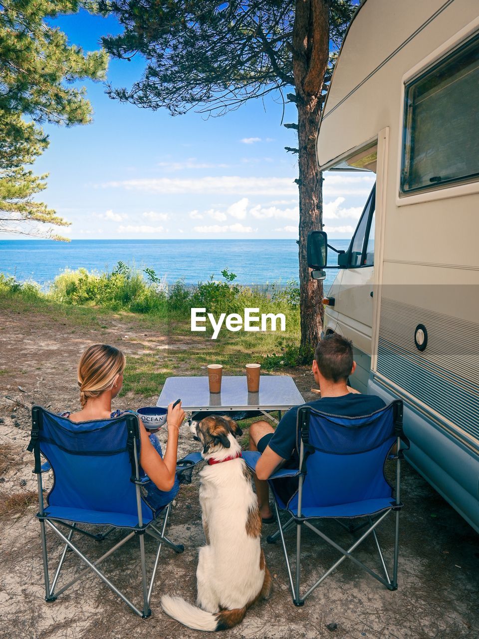 A young couple a d dog eating in front of the motorhome. sea view