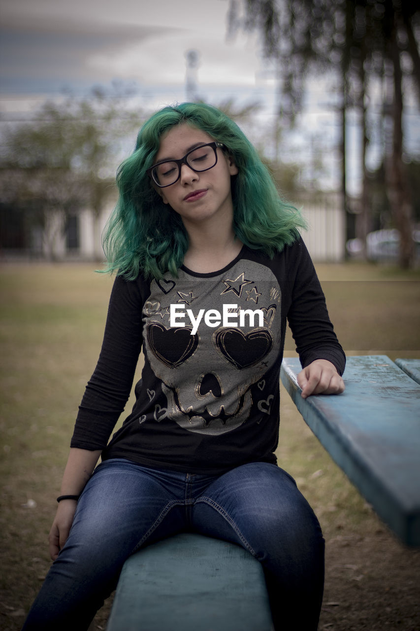 Beautiful young woman with eyes closed sitting on bench by table