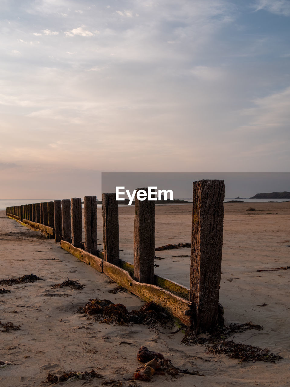 WOODEN POSTS ON BEACH BY SEA AGAINST SKY