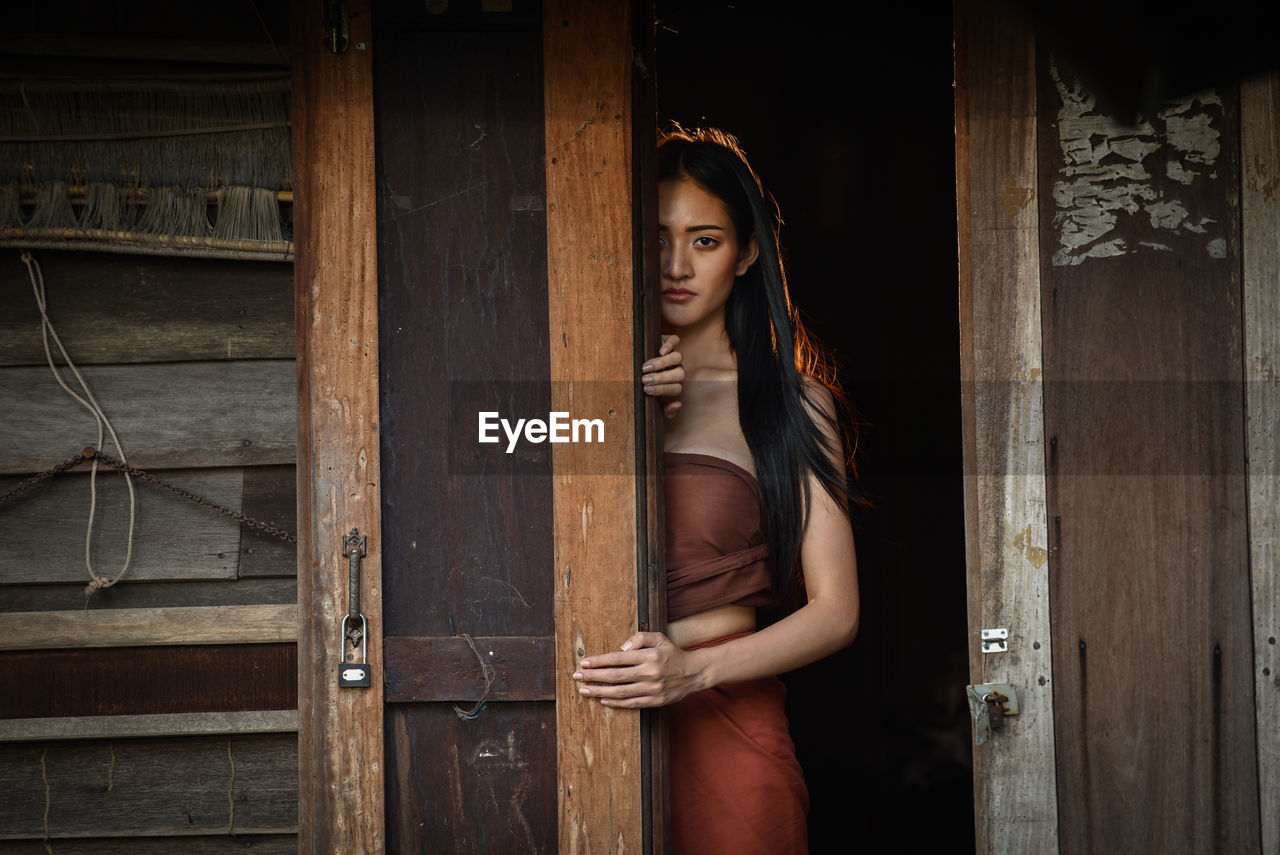 Portrait of young woman standing by wooden door