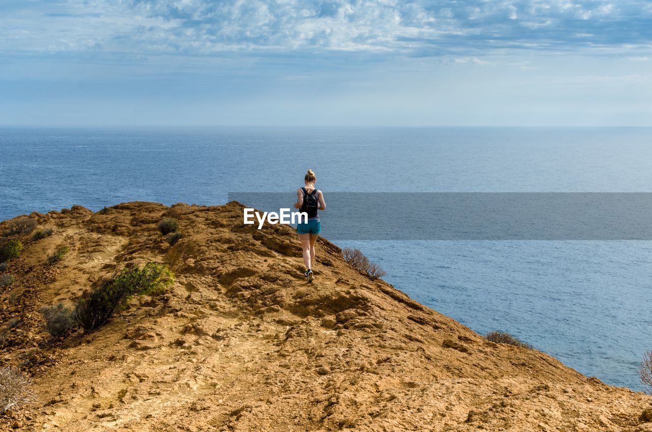 Rear view of woman walking on rock by sea against sky