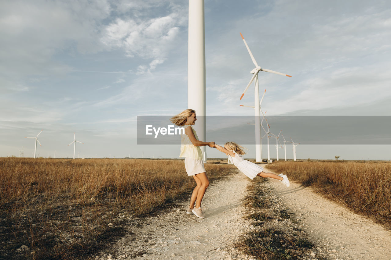 Cheerful mother spinning daughter in front of wind turbines