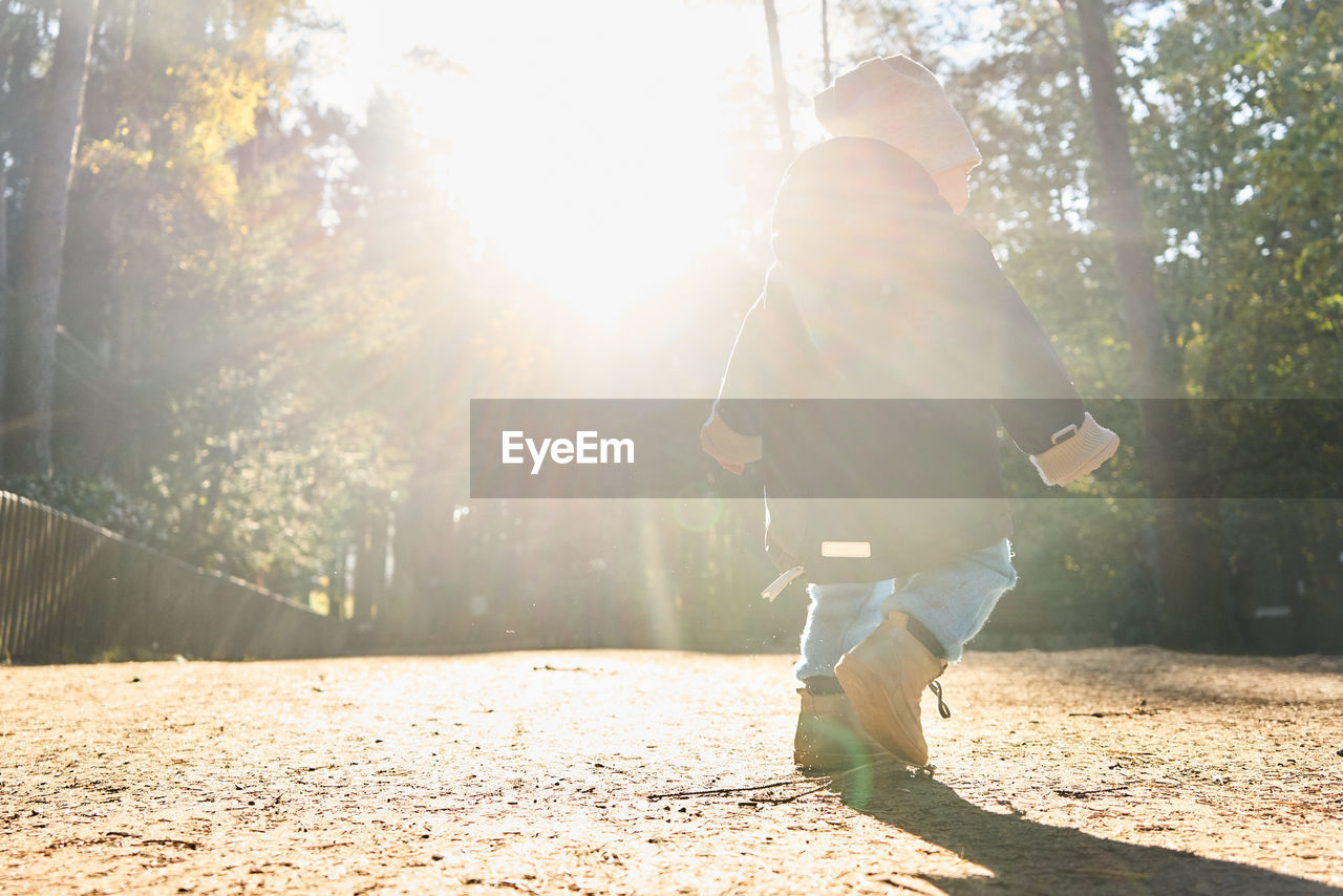 REAR VIEW OF WOMAN WALKING AGAINST BRIGHT SUN