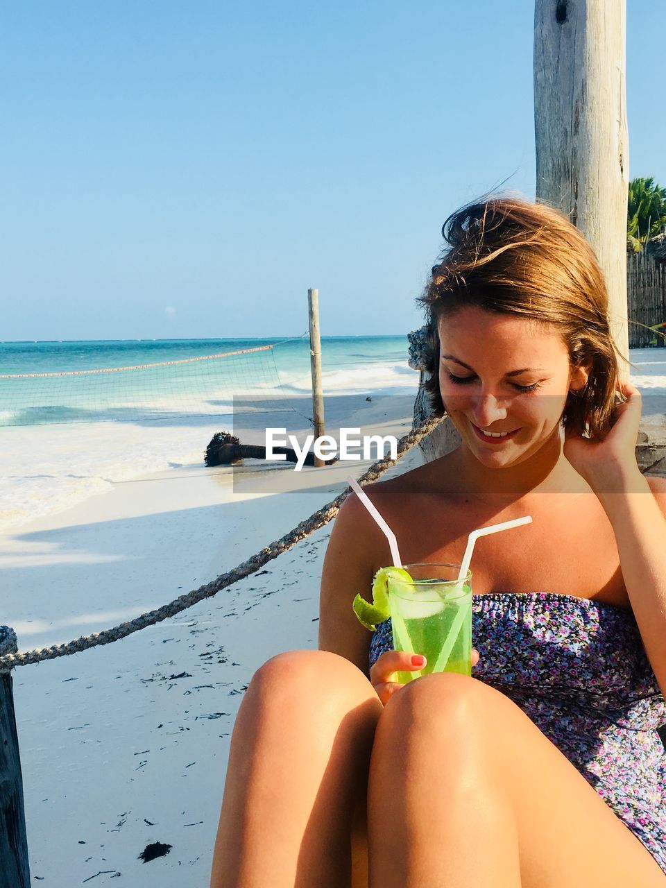 YOUNG WOMAN SITTING ON BEACH AGAINST SEA