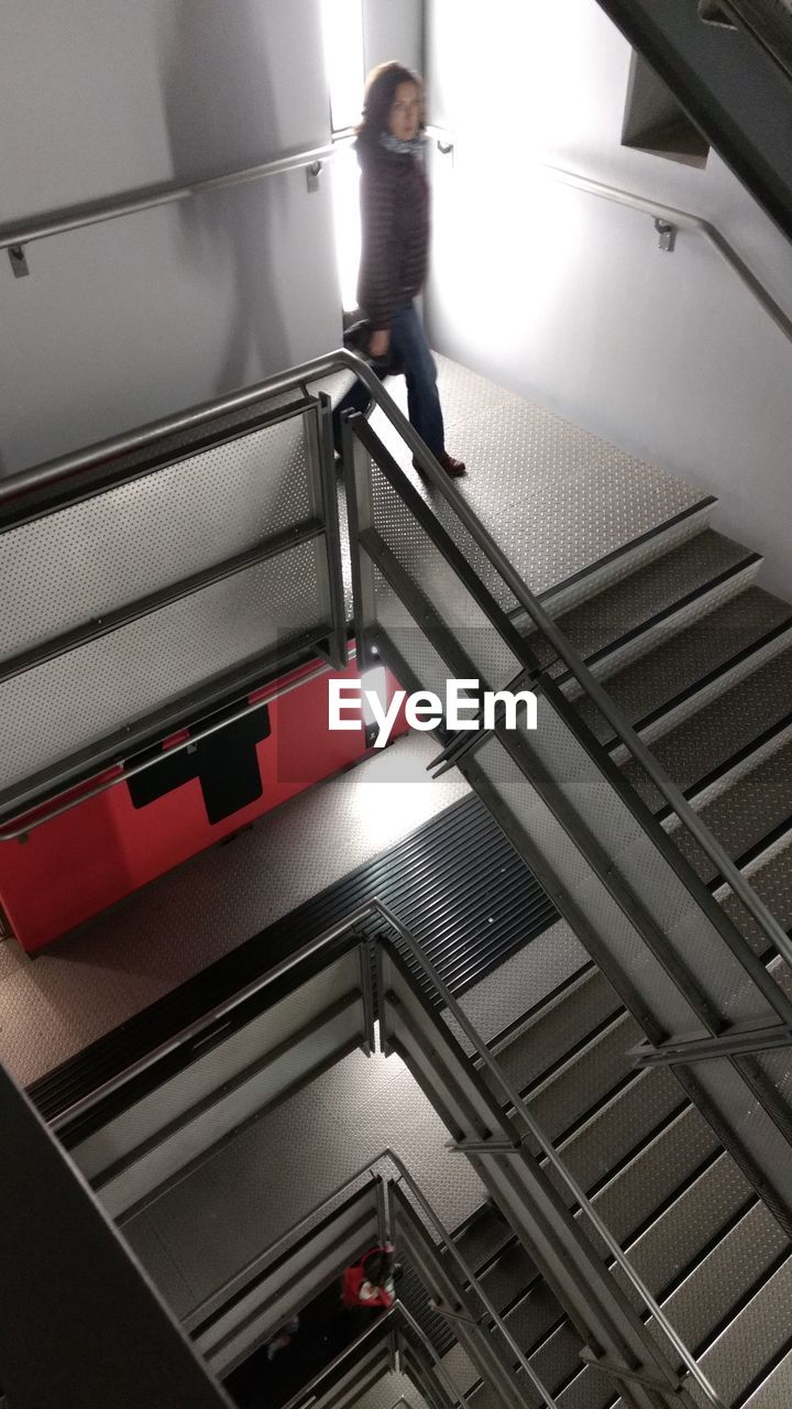 LOW ANGLE VIEW OF WOMAN STANDING ON STAIRCASE