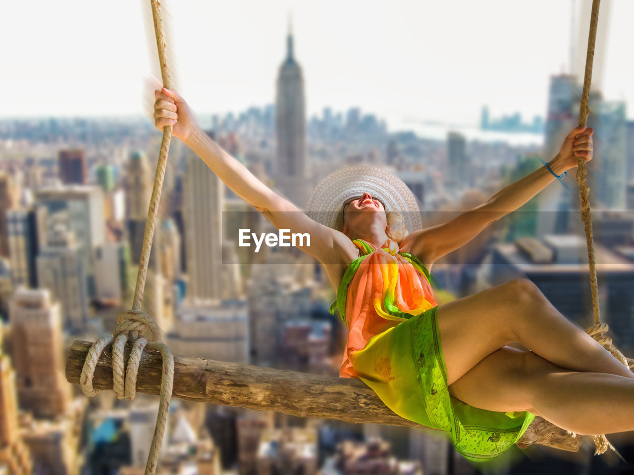 Happy woman on swing against cityscape