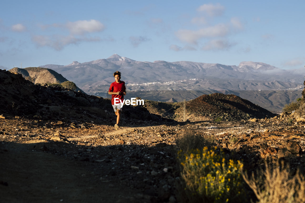 REAR VIEW OF PERSON ON MOUNTAIN AGAINST SKY