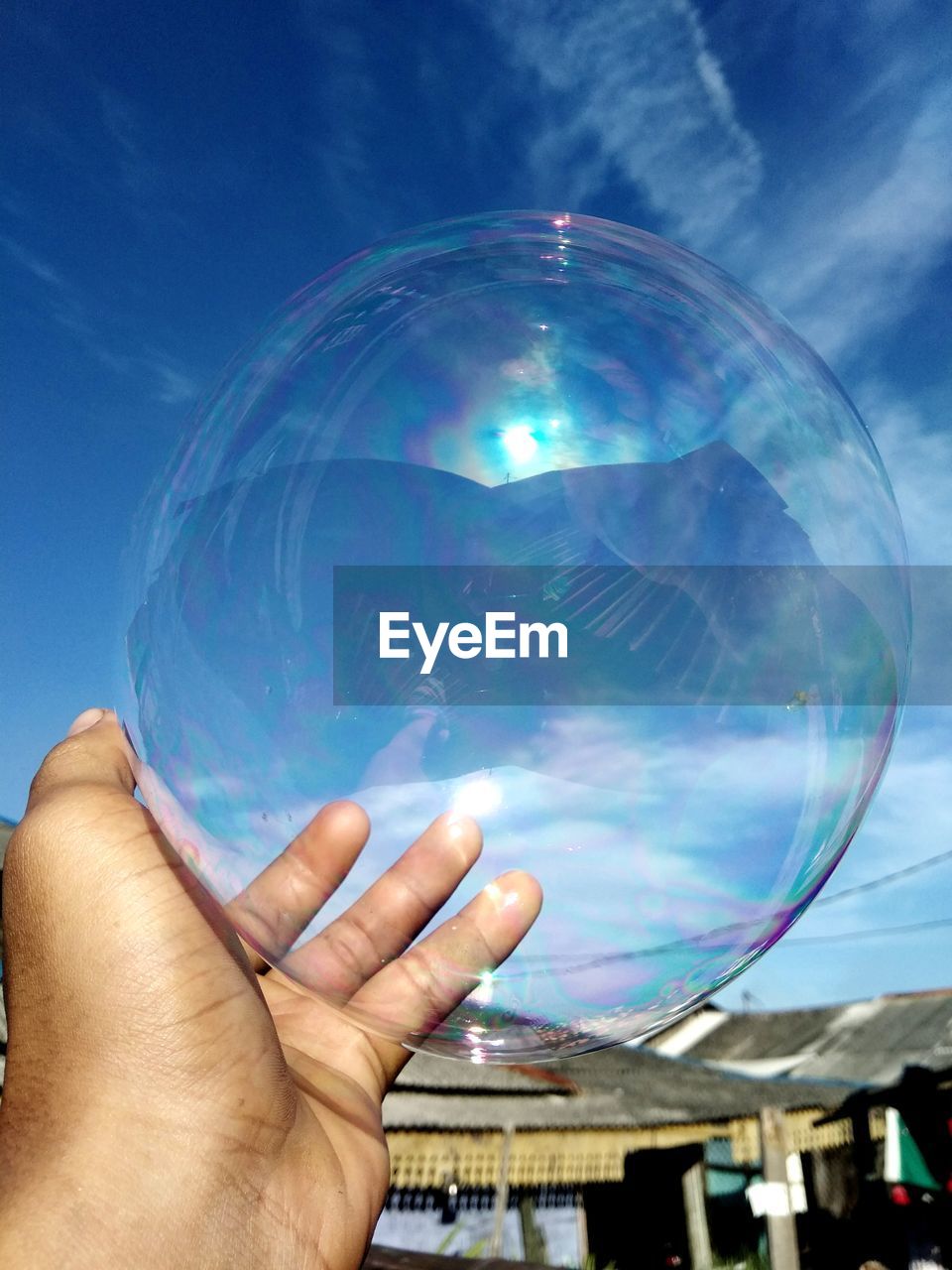 Cropped image of person hand holding bubble against sky