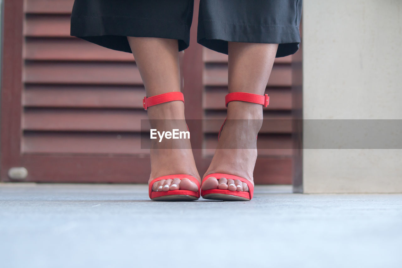 Low section of woman wearing red high heels on floor