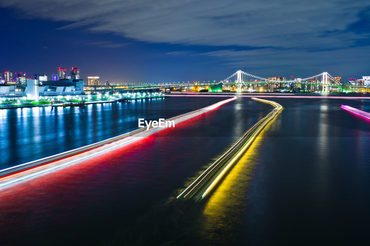 Illuminated city by river against sky at night