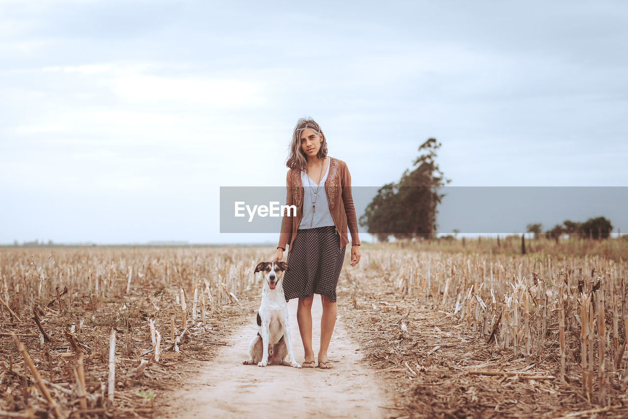 Full length portrait of young woman standing on field against sky