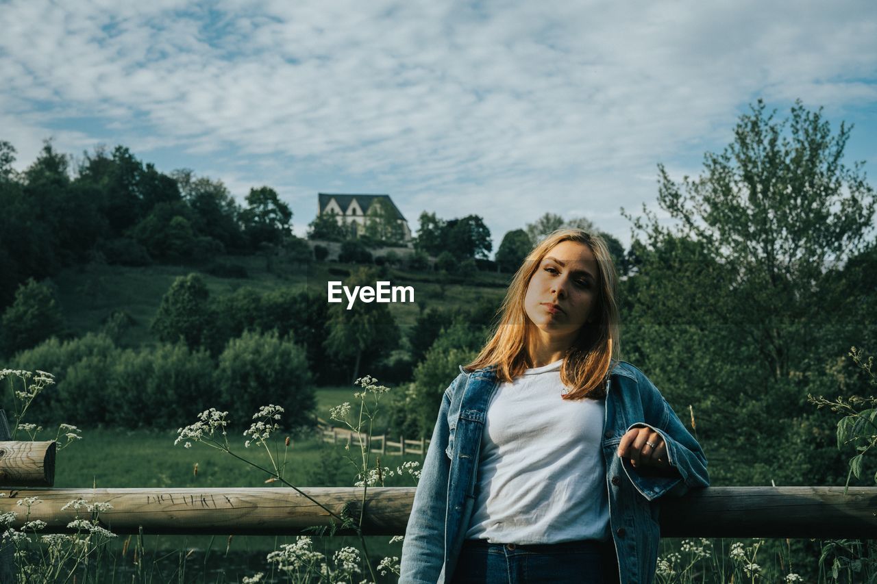 Portrait of beautiful young woman standing against trees