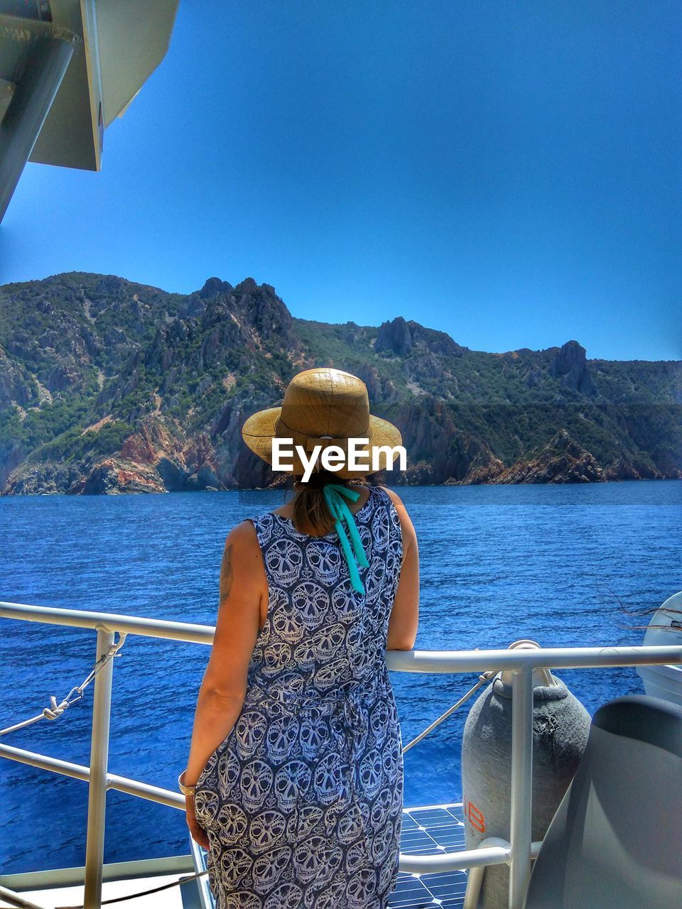 Rear view of woman standing by railing of boat on sea against clear blue sky