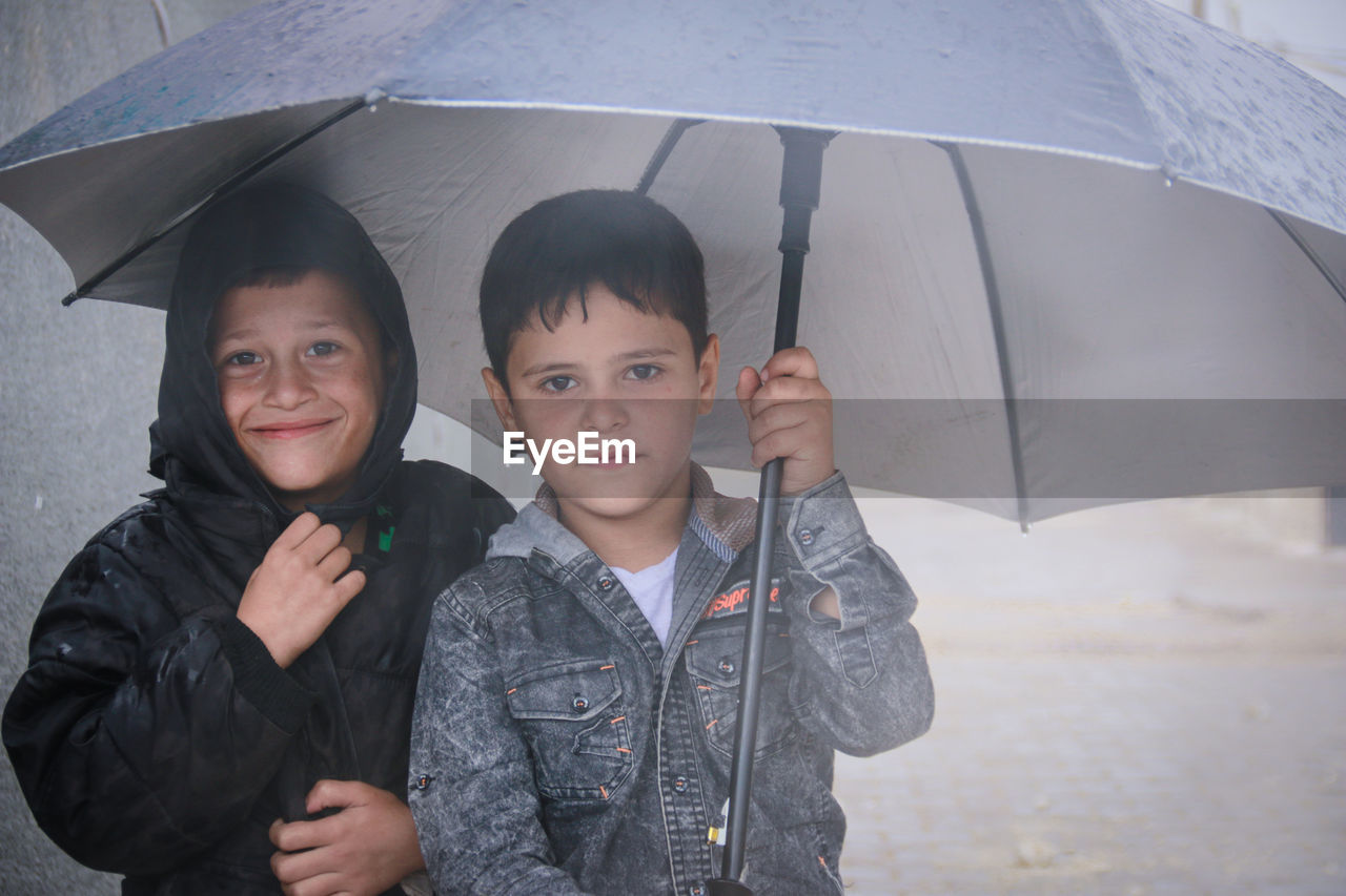 Little refugee children with umbrella in the rain, refugee with umbrella.