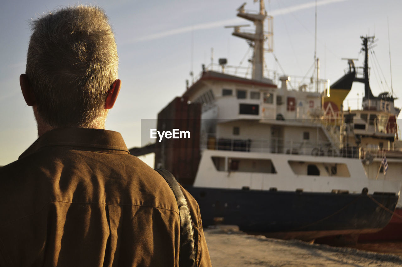 REAR VIEW OF MAN LOOKING AT VIEW OF BOAT