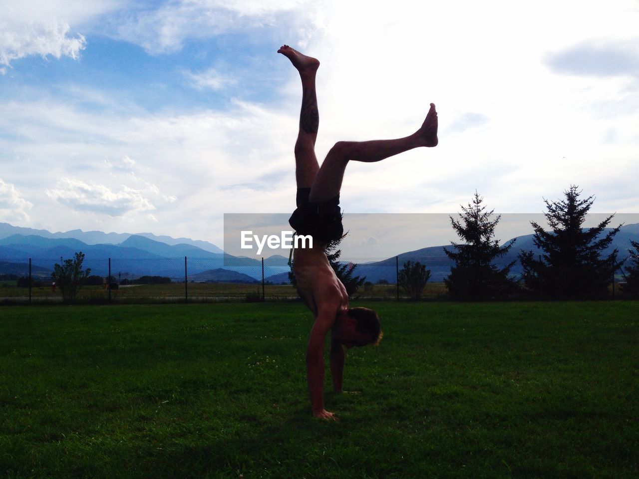 Full length of shirtless man doing handstand on field against sky