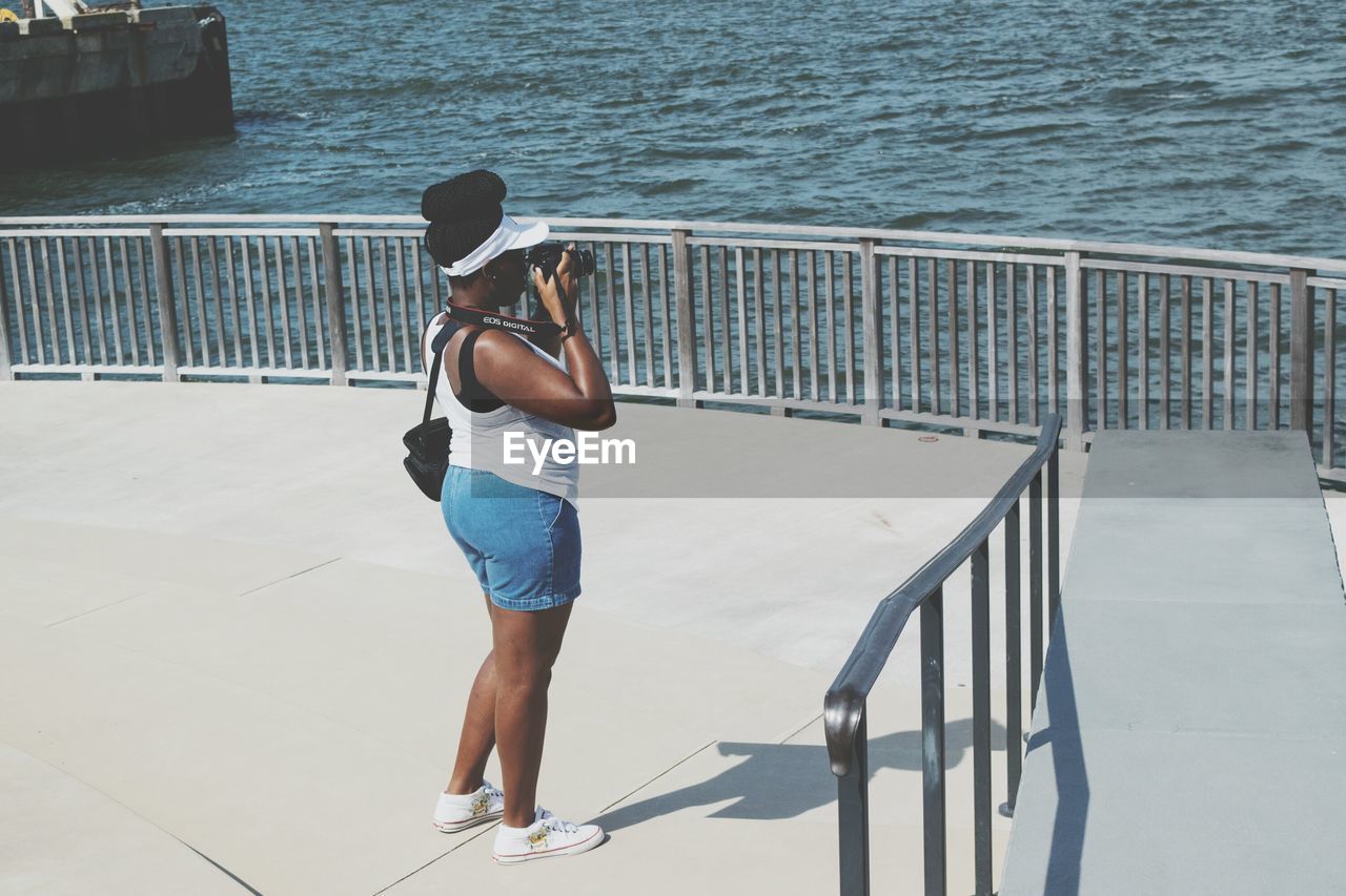 REAR VIEW OF MAN STANDING ON PIER BY SEA