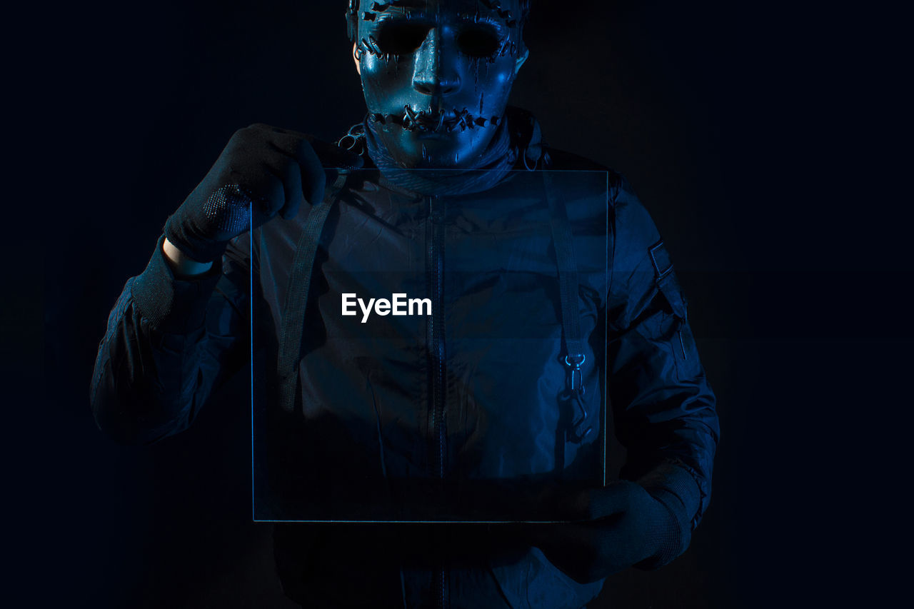 PORTRAIT OF YOUNG MAN WEARING MASK AGAINST BLACK BACKGROUND