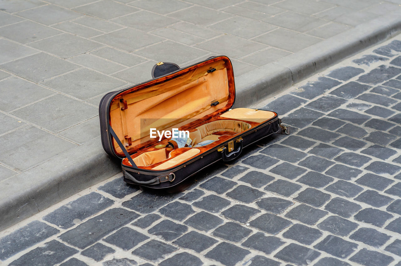 Open violin case lies on old cobblestone in city. street musician collects money