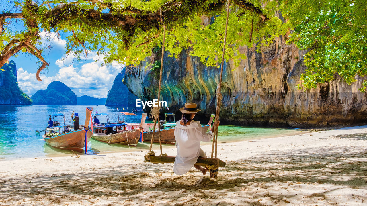 rear view of woman sitting on swing at beach