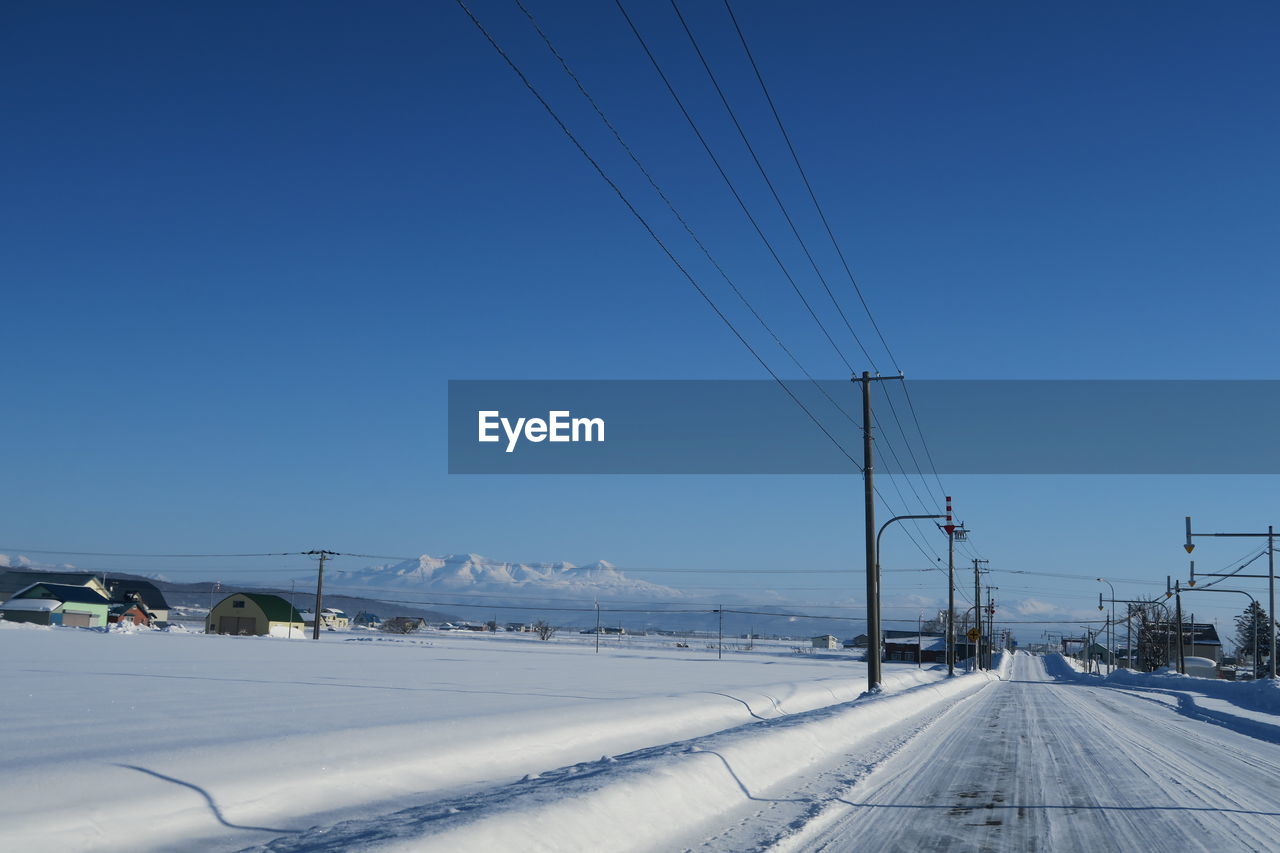 Road by snow covered landscape against clear blue sky