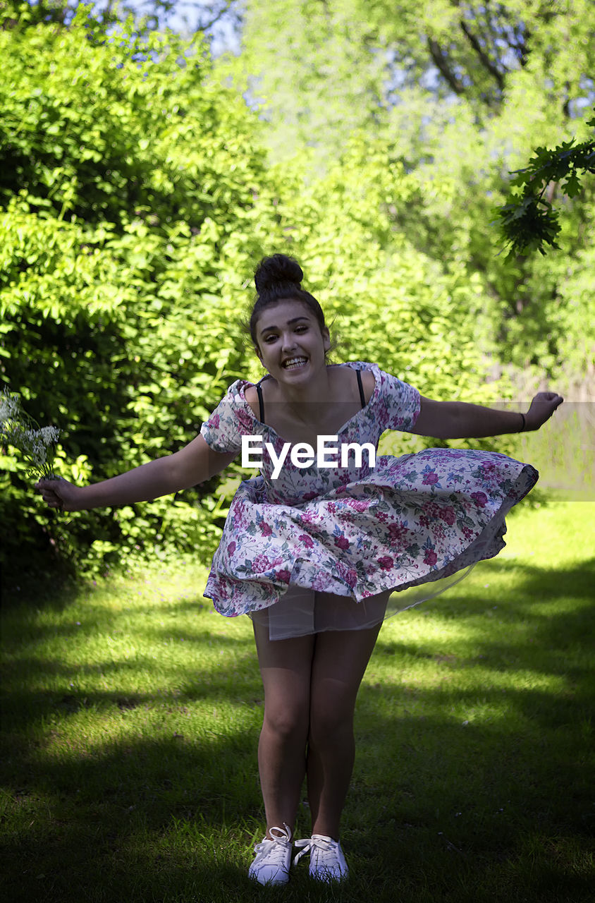 Portrait of smiling woman holding flower while standing on grass