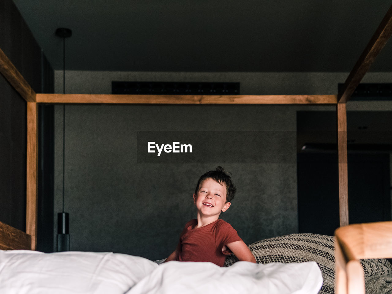 Positive little kid on wooden canopy bed while having fun in bedroom and looking at camera