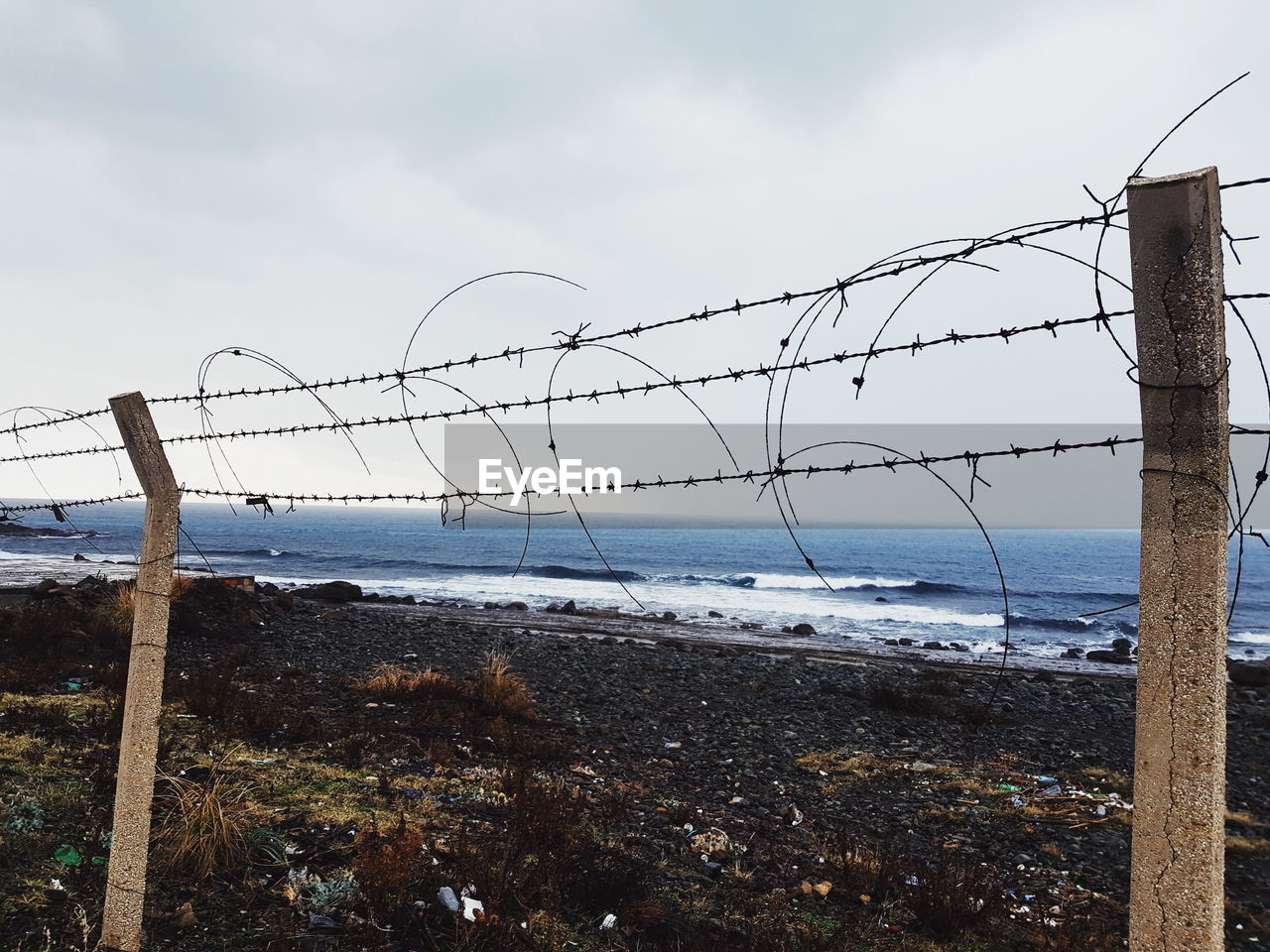 BARBED WIRE FENCE ON SHORE AGAINST SKY