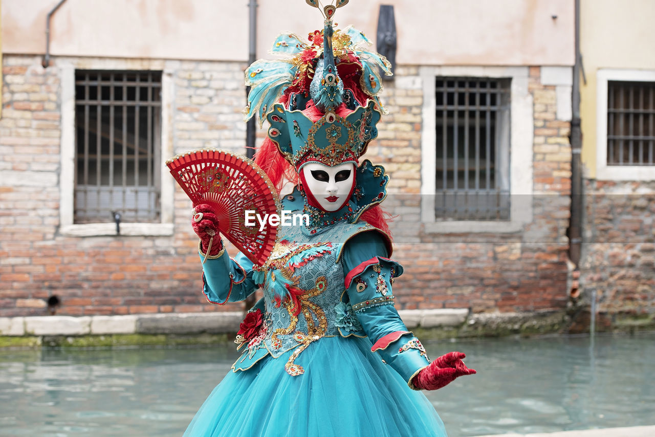 Woman in carnival costume standing by canal in city