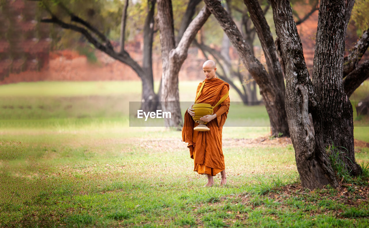 Monk carrying container while standing on land