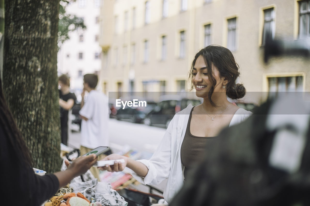 Smiling female owner taking mobile payment from customer doing shopping at market