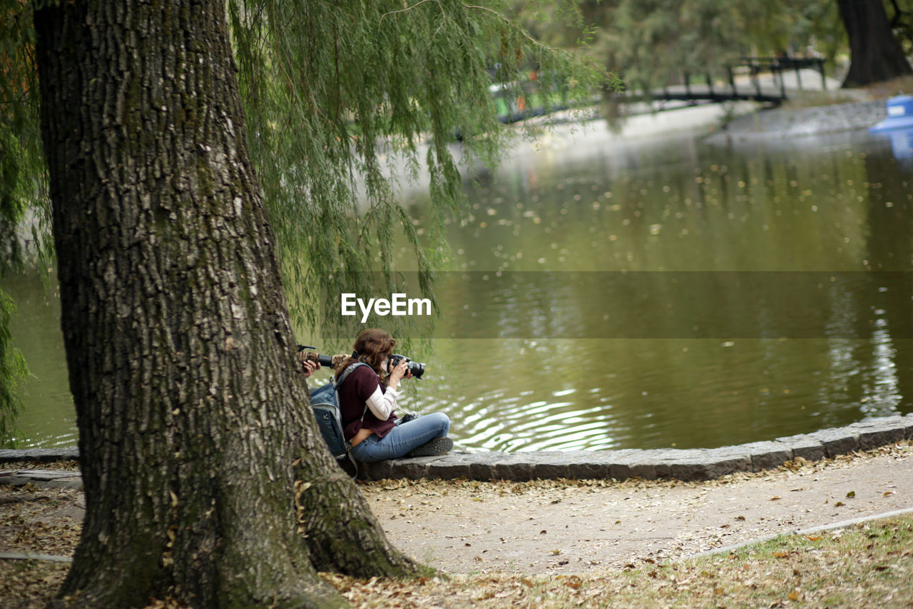 MAN SITTING ON BENCH BY TREE TRUNK