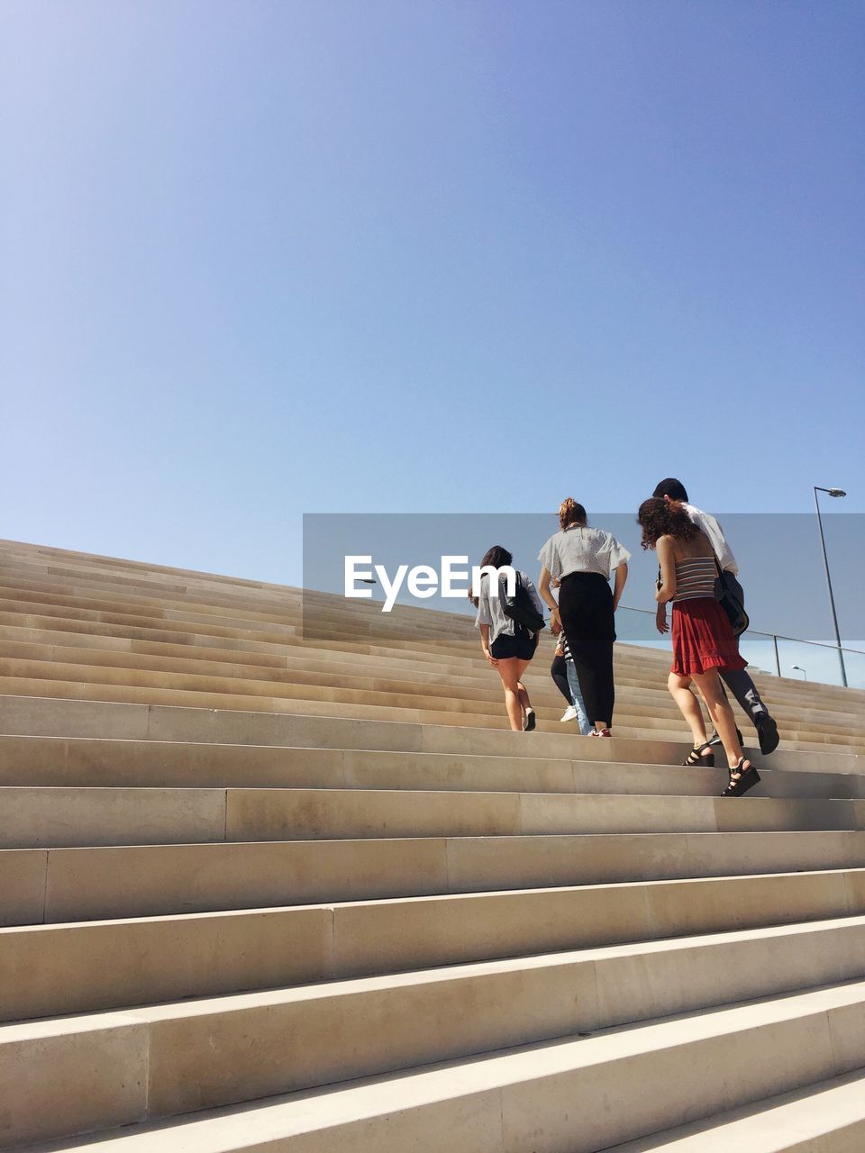 Low angle view of friends walking on staircase against clear blue sky
