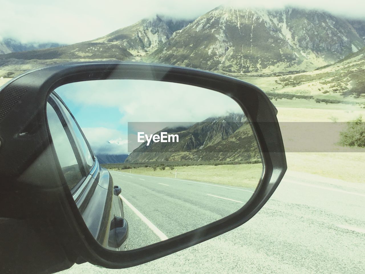 REFLECTION OF ROAD ON SIDE-VIEW MIRROR AGAINST SKY